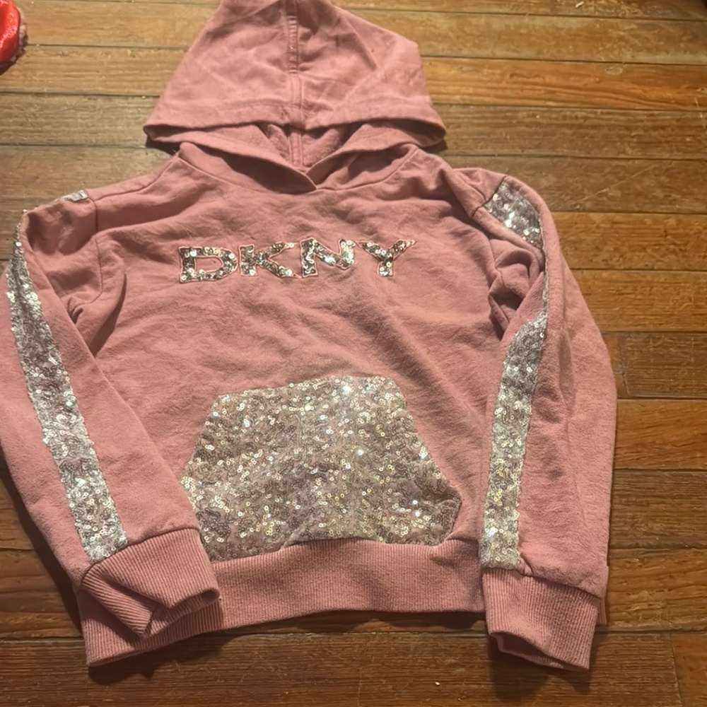 This stylish DKNY hoodie for kids features a beautiful pink color with sparkling